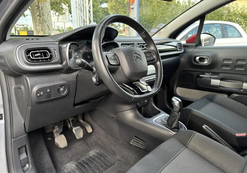 Intérieur de Citroën C3 2019 côté conducteur, volant multifonction, levier de vitesse manuel et sièges noirs.