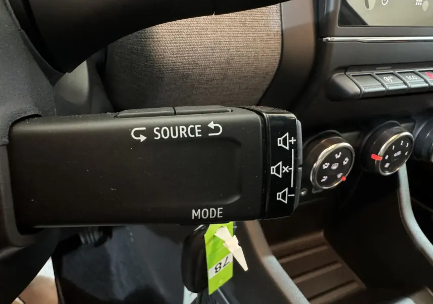 Gros plan sur la commande audio au volant noir de la Renault Clio gris clair, avec tableau de bord et boutons de climatisation visibles.