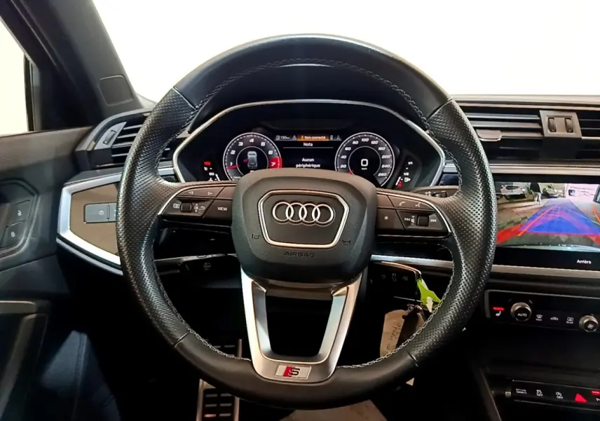 Vue intérieure centrée sur le volant cuir perforé S Line d’un Audi Q3 35 TFSI 150 S Tronic avec tableau de bord digital.