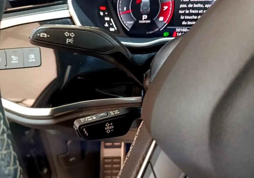 Gros plan sur la commande de régulateur de vitesse et clignotants du volant cuir noir de l'Audi Q3 gris foncé 2022.