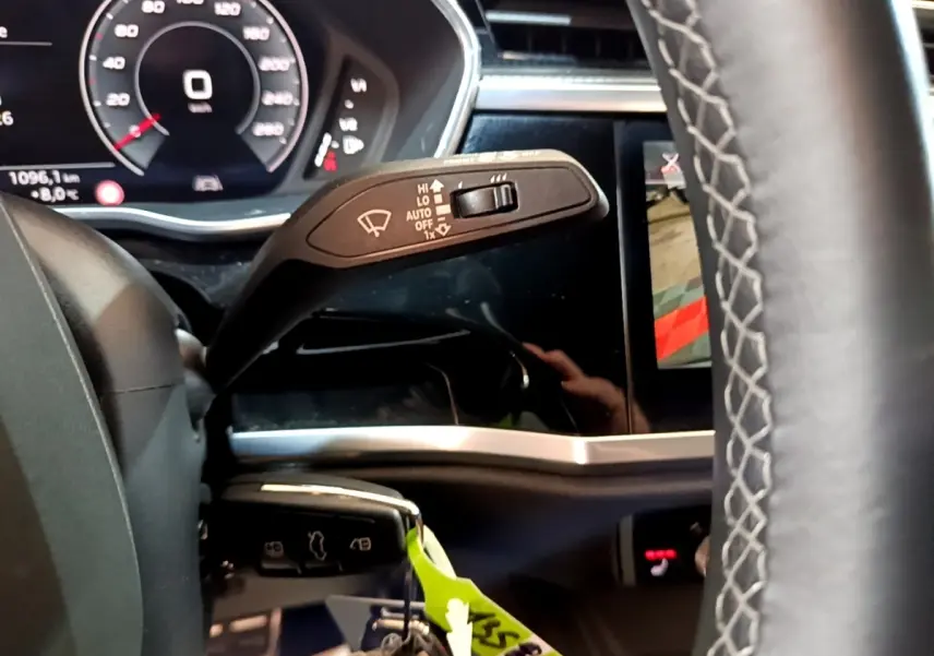 Gros plan sur la manette d’essuie-glace à gauche du volant cuir de l’Audi Q3 gris foncé, tableau de bord digital visible.