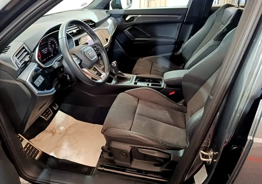 Vue intérieure côté conducteur de l’Audi Q3 gris foncé 35 TFSI S Line, avec volant cuir multifonctions et sièges tissu.