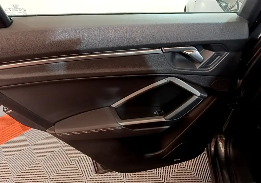 Vue intérieure côté gauche de la porte avant d'un Audi Q3 gris foncé avec garniture noire et insert argenté.