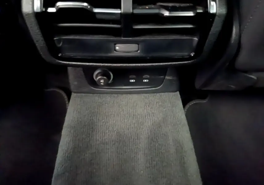 Vue intérieure centrée sur la console arrière noire avec prise 12V et aérateurs dans un Audi Q3 gris foncé.