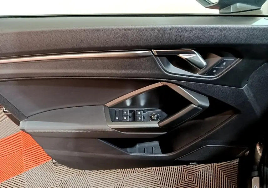 Gros plan sur la porte côté gauche de l'Audi Q3 gris foncé, avec commandes de vitres et poignée argentée.