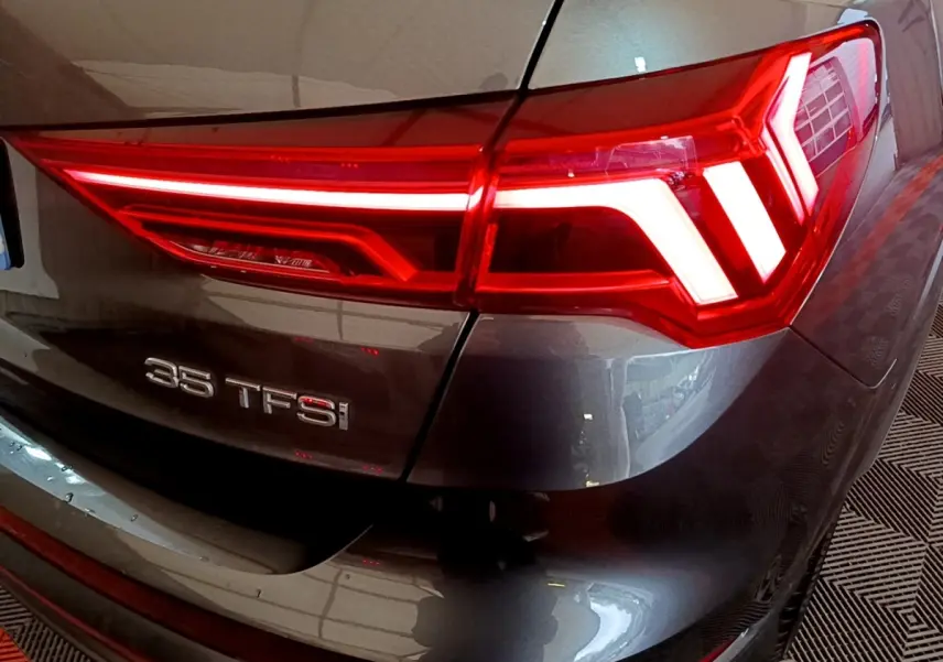 Gros plan sur le feu arrière droit rouge et le badge 35 TFSI d’un Audi Q3 gris foncé 2022.