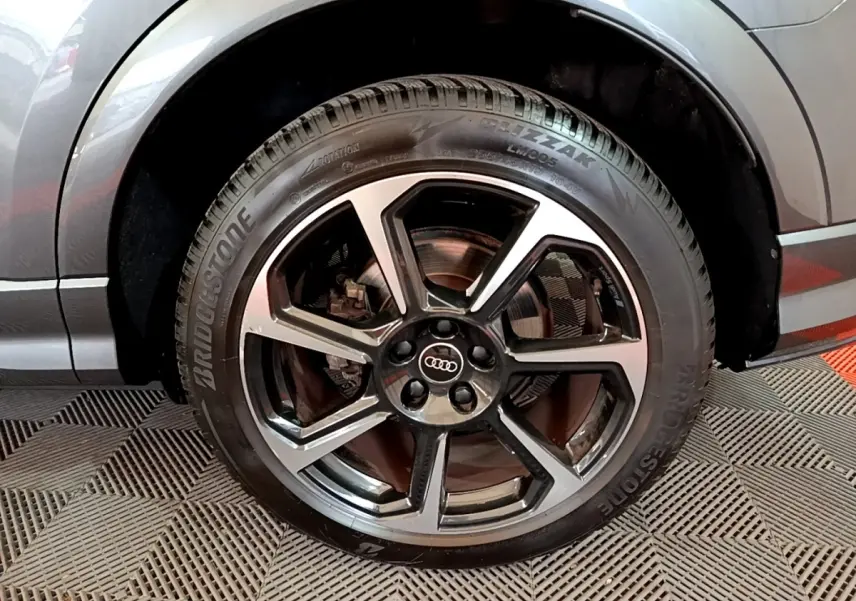 Gros plan sur la roue avant droite d’un Audi Q3 gris foncé avec jante alliage noir et argent.
