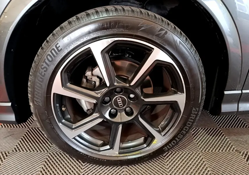 Gros plan sur la roue avant droite d’un Audi Q3 gris foncé avec jante alliage noir et argent et pneu Bridgestone.