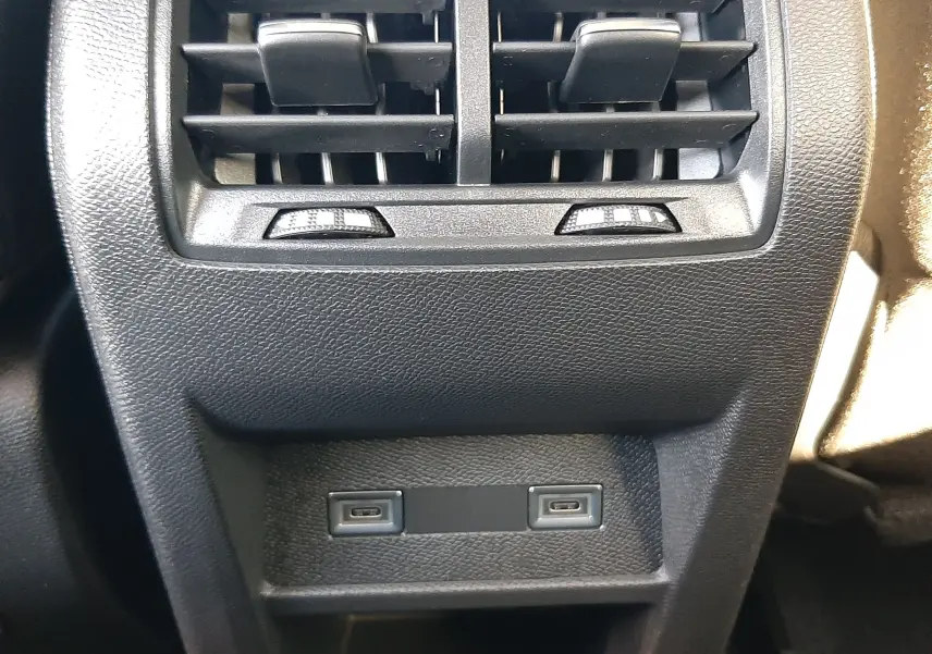 Vue plongeante sur l'accoudoir central noir et les sièges gris avec surpiqûres vertes de la Peugeot 308 2026.