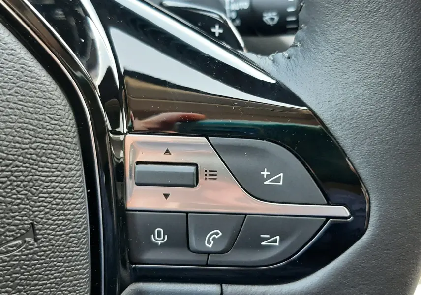 Gros plan sur les commandes de régulateur de vitesse au volant noir de la Peugeot 308 Bleu Obsession 2026.