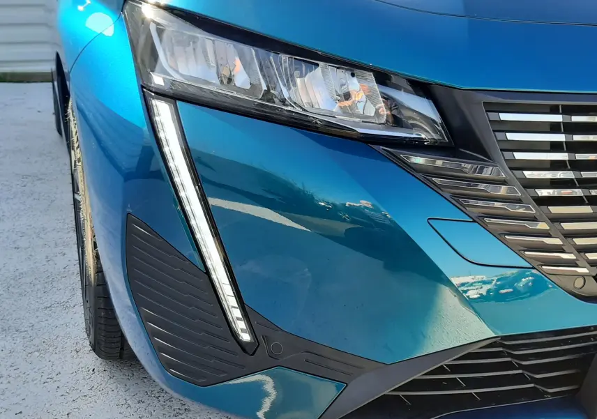Vue 3/4 avant droit d'une Peugeot 308 Bleu Obsession avec rétroviseur noir brillant et vitres teintées.