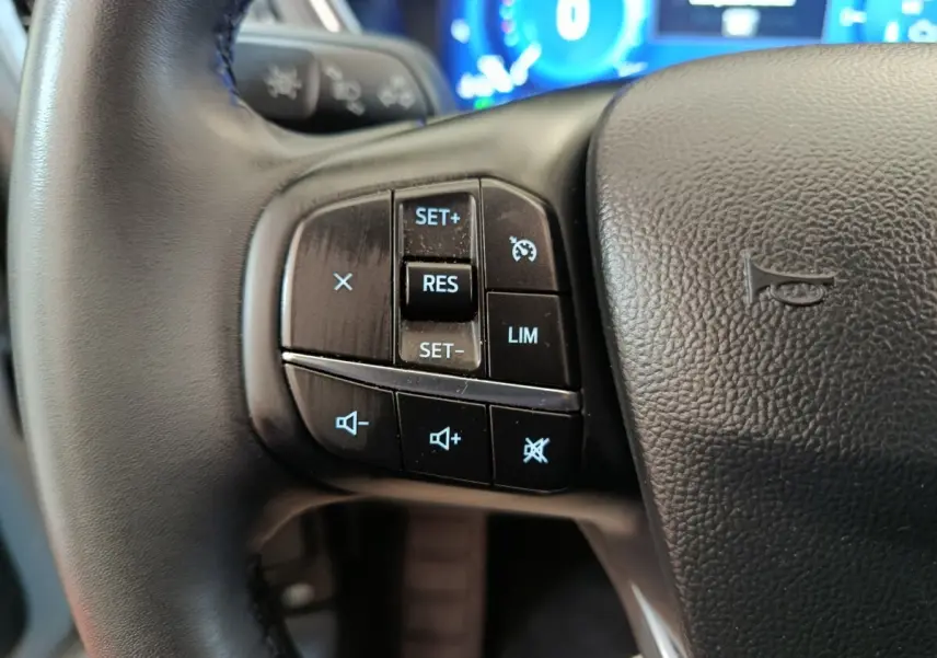 Gros plan sur les commandes du régulateur de vitesse au volant cuir noir du Ford Kuga gris foncé 2023.