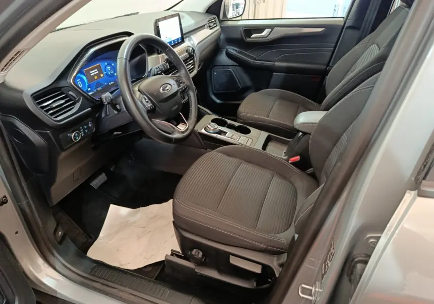 Vue intérieure côté conducteur du Ford Kuga gris foncé 2023, avec tableau de bord numérique et volant multifonctions cuir.