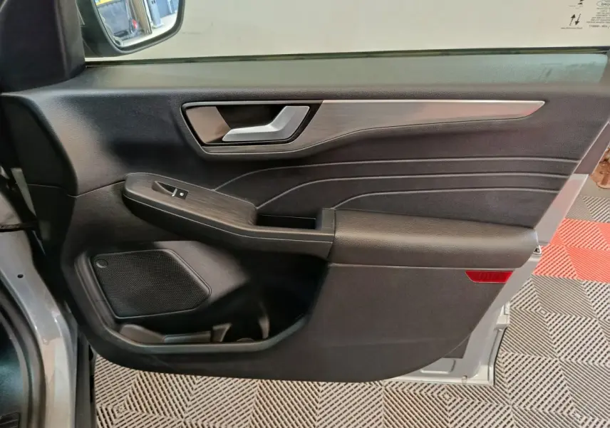 Vue intérieure côté gauche de la porte avant d’un Ford Kuga gris foncé avec garniture noire et insert décoratif métallique.