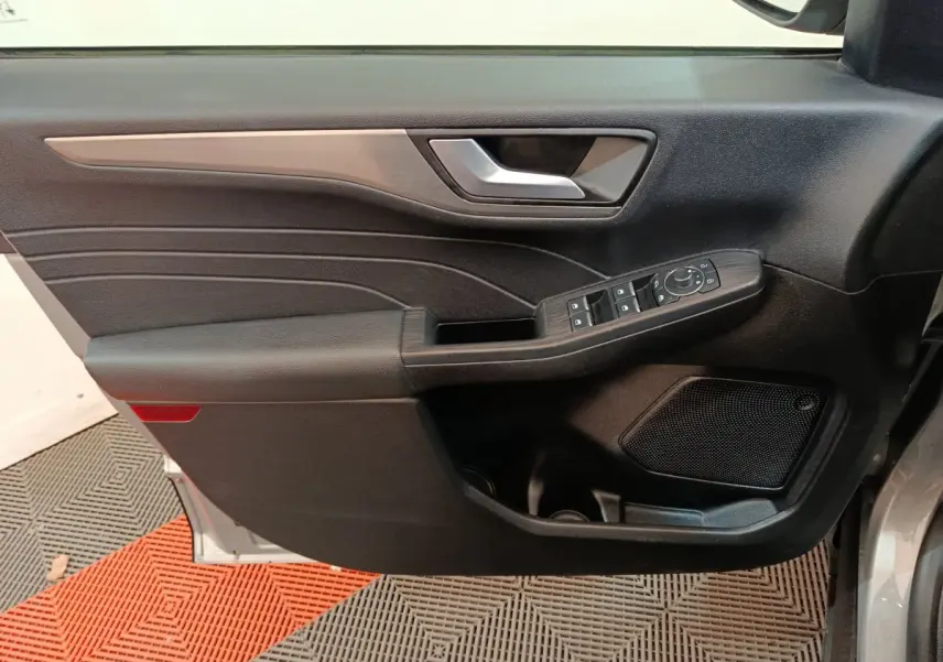 Vue intérieure côté gauche de la porte avant d’un Ford Kuga gris foncé avec commandes de vitres et haut-parleur intégré.