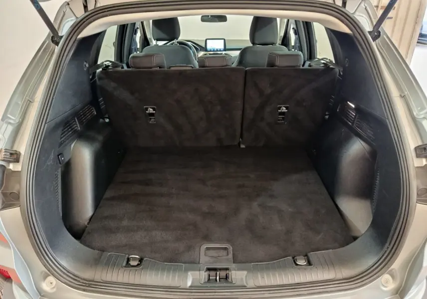 Vue du coffre ouvert d'un Ford Kuga gris foncé 2023, montrant l'espace de chargement et les sièges arrière rabattus.