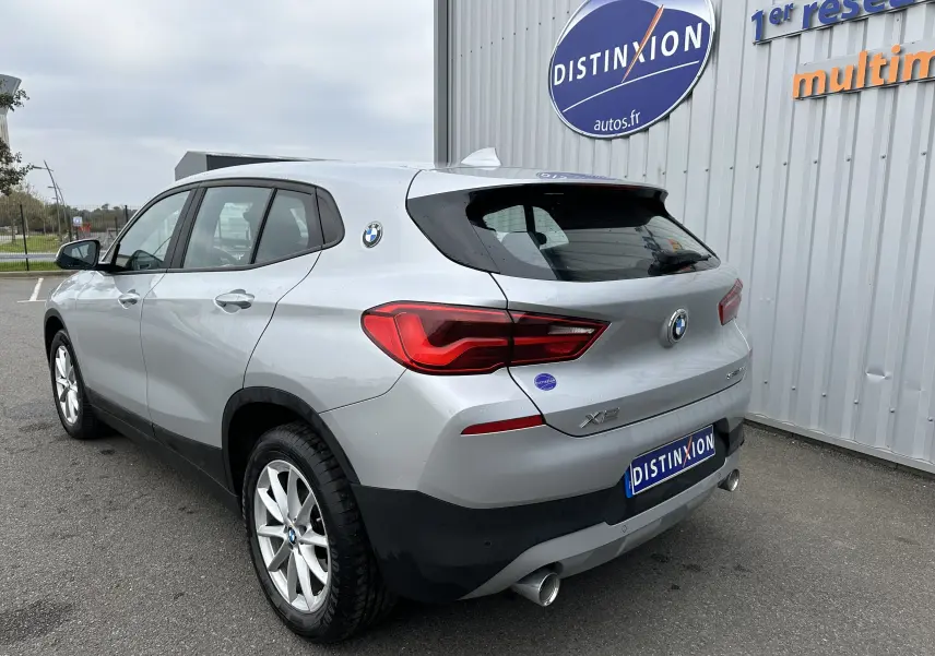 Vue 3/4 arrière droite d'un BMW X2 gris 2018 avec feux LED et double sortie d'échappement visible.