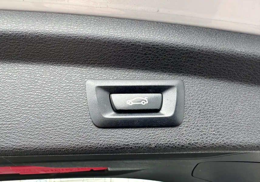 Bouton de déverrouillage du hayon sur la garniture intérieure noire du coffre d'un BMW X2 gris 2018.
