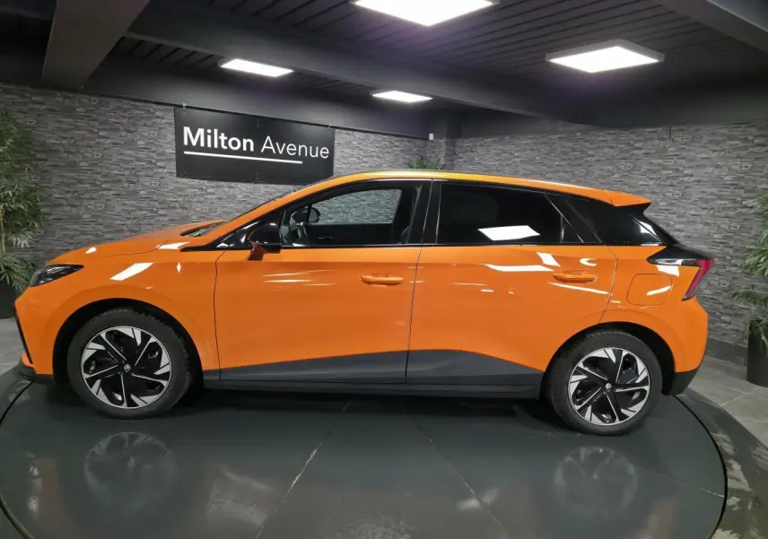 Profil droit d'une MG4 électrique orange avec toit noir et jantes alliage bi-ton dans un showroom intérieur.