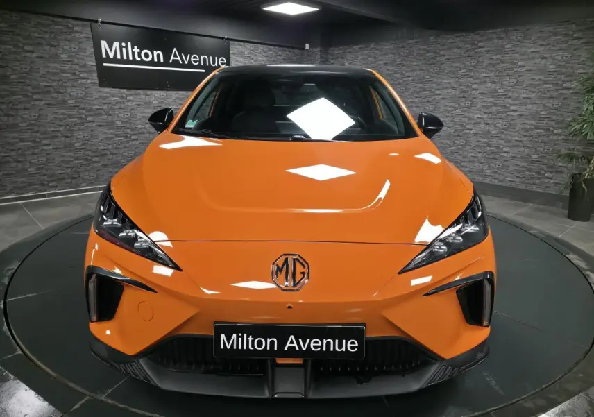 Vue avant d'une MG4 électrique orange avec calandre noire et logo MG centré, en showroom Milton Avenue.
