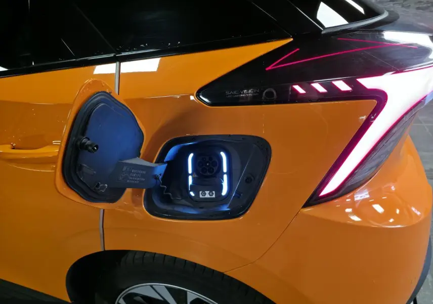 Prise de recharge ouverte côté arrière droit d'une MG4 orange avec feux arrière LED en forme de flèche.