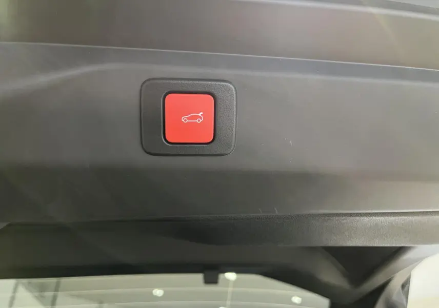 Bouton rouge d'ouverture électrique du hayon sur la garniture intérieure du coffre du Peugeot 3008 gris titanium.