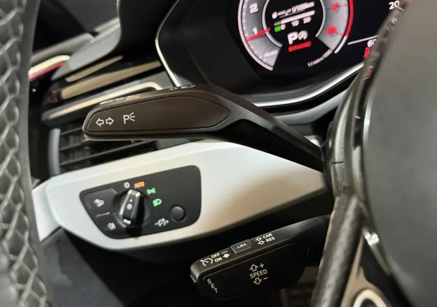 Gros plan sur la commande de clignotants et le tableau de bord numérique de l’Audi A4 gris foncé, côté gauche du volant.