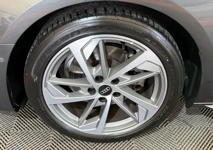 Gros plan sur la jante alliage argentée de l'Audi A4 gris foncé, montrant le logo Audi au centre.