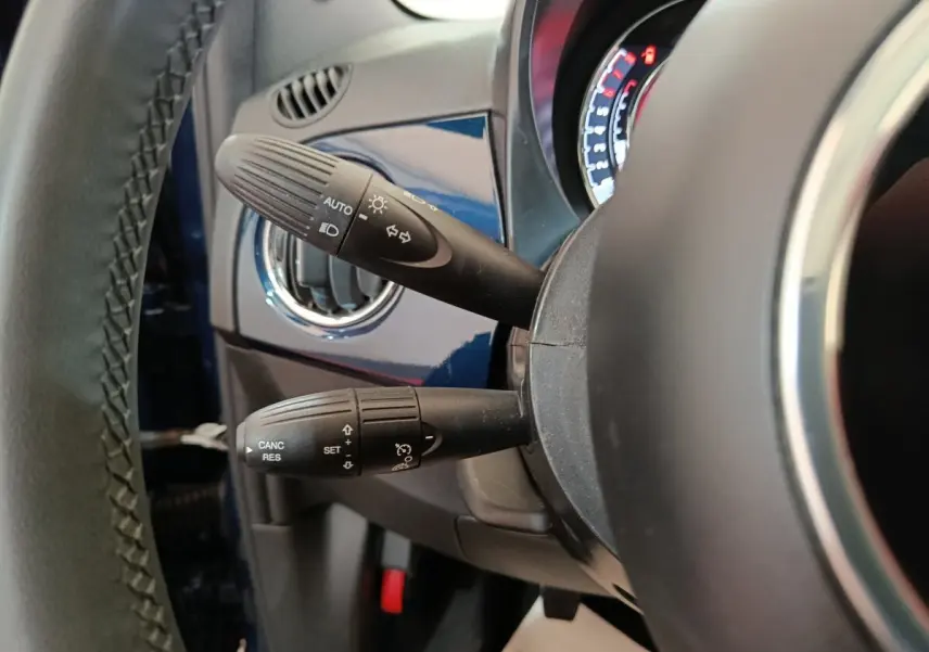 Détail intérieur côté gauche du volant cuir d’une FIAT 500 Dolcevita bleu, avec commandes de phares et régulateur.