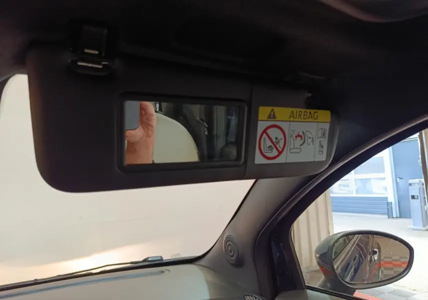 Vue intérieure côté conducteur du pare-soleil avec miroir et avertissement airbag, rétroviseur extérieur bleu visible.