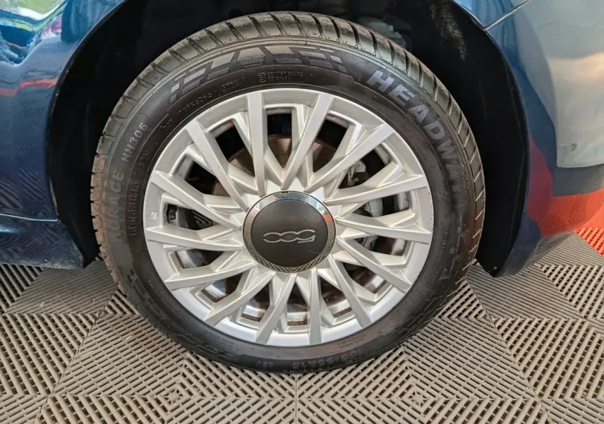 Gros plan sur la roue arrière droite d'une FIAT 500 Hybrid bleu, avec partie de la carrosserie visible.