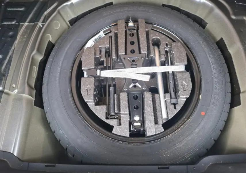 Vue plongeante sur la roue de secours et son kit d'outils dans le coffre du Skoda Kamiq gris foncé 2024.