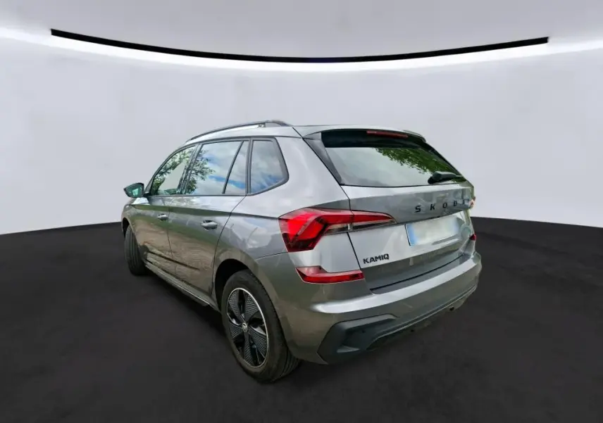Vue 3/4 arrière gauche d’un Skoda Kamiq gris foncé 2024 avec feux arrière LED et jantes alliage noires.