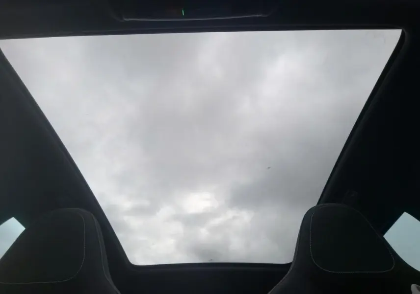 Vue intérieure du toit panoramique du Skoda Kamiq 2024 gris foncé, avec sièges avant en tissu noir visibles en partie.