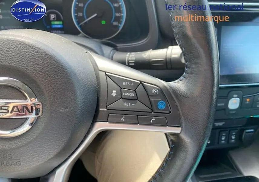 Vue rapprochée du volant en cuir noir de la Nissan Leaf électrique blanche nacrée, avec commandes intégrées visibles.