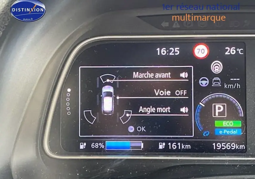 Tableau de bord numérique de Nissan Leaf blanche nacrée, affichant l'état de conduite et l'autonomie à 68% batterie.