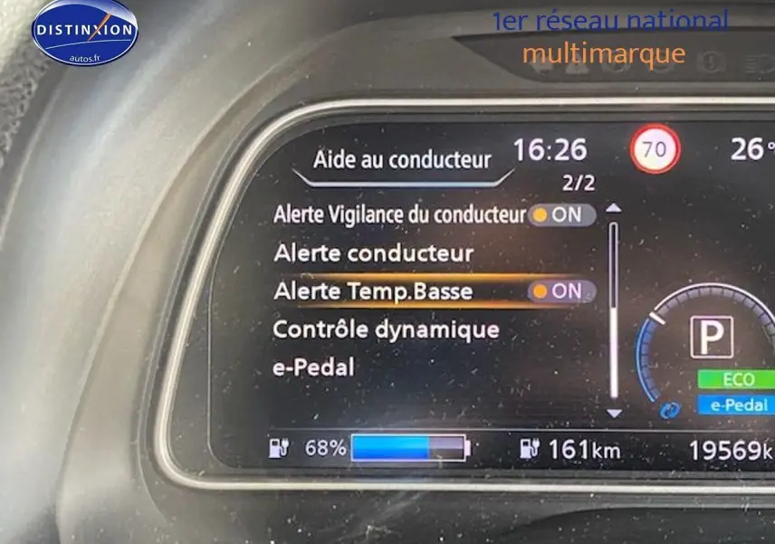 Tableau de bord numérique de Nissan Leaf blanche nacrée, affichant alertes et autonomie à 68% de charge.