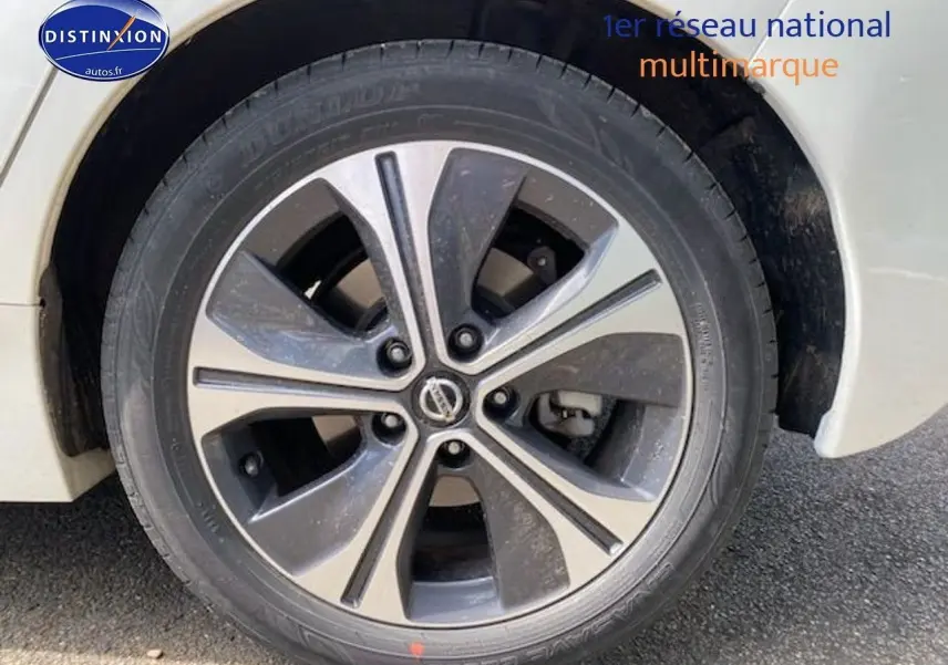 Gros plan sur la roue avant gauche d'une Nissan Leaf électrique 2019 blanc nacré avec jante alliage bicolore.