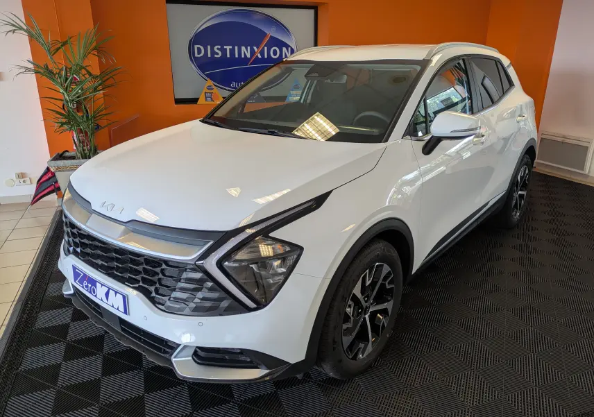 Vue 3/4 avant droite d’un KIA Sportage blanc 2025 avec jantes alliage 18’’ et calandre distinctive en showroom.