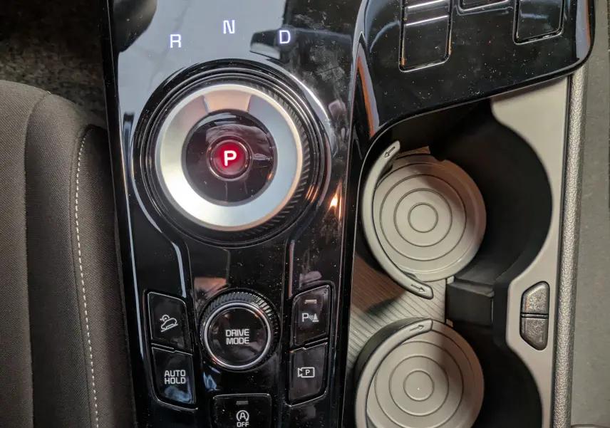 Vue rapprochée de la console centrale noire du Kia Sportage MY25 avec sélecteur rotatif de boîte auto et porte-gobelets.