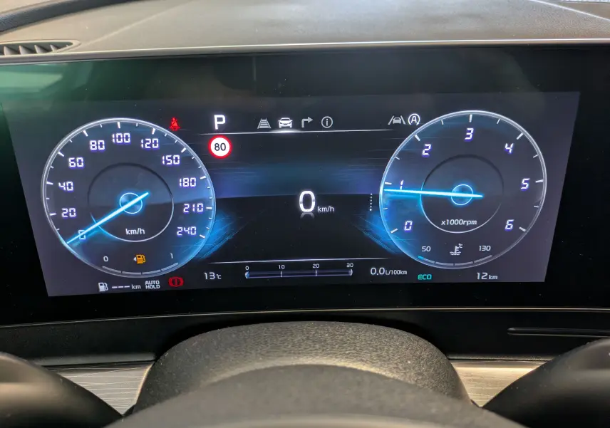 Tableau de bord numérique du Kia Sportage blanc MY25, affichant vitesse, régime et alertes à 0 km/h.