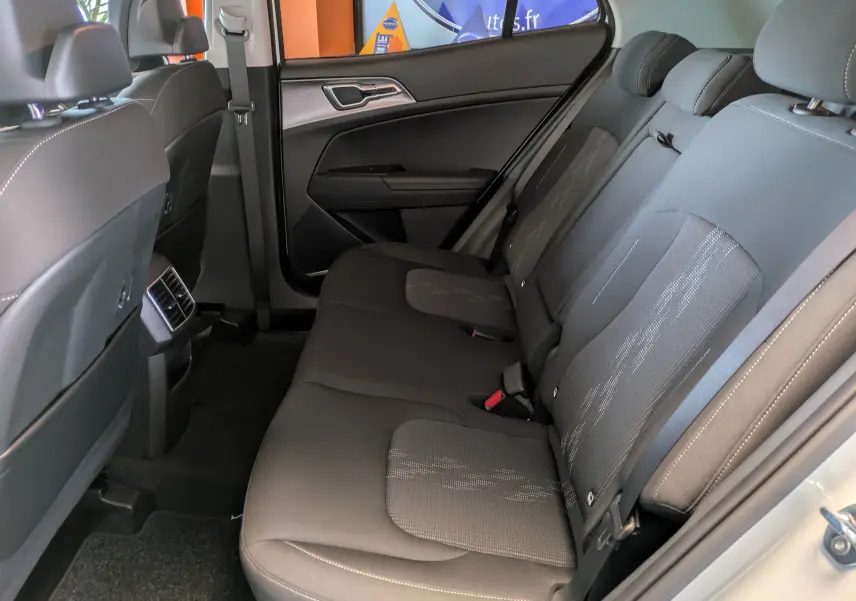 Vue intérieure arrière côté droit du Kia Sportage blanc MY25, sièges tissu gris foncé avec surpiqûres claires.