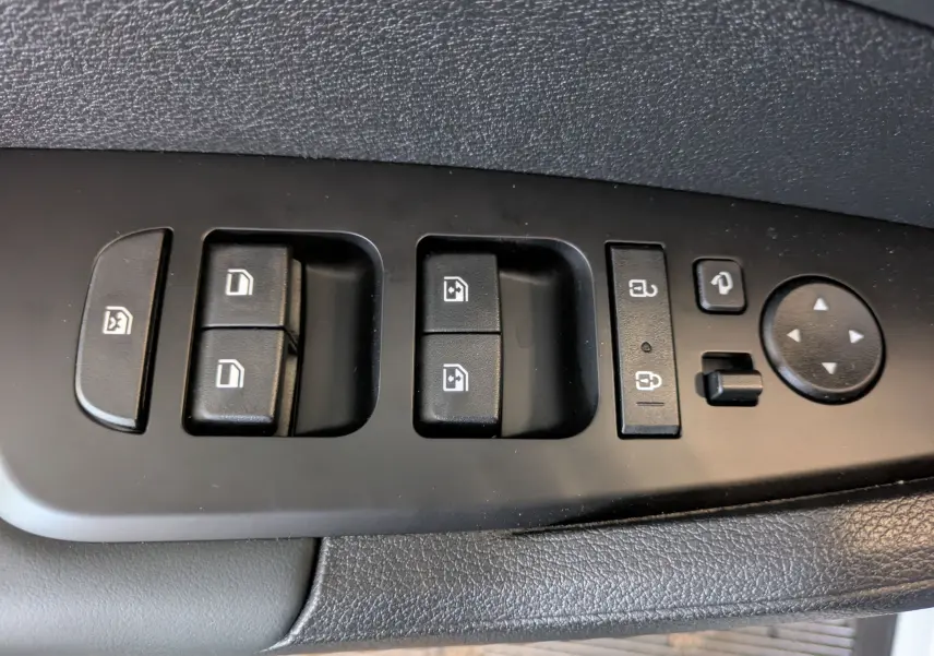 Gros plan sur les commandes de lève-vitres et réglages des rétroviseurs côté conducteur du Kia Sportage blanc MY25.