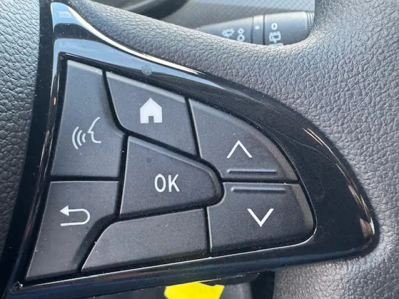 Gros plan sur les commandes noires au volant côté gauche du Dacia Sandero blanc 2024, boutons multifonctions visibles.