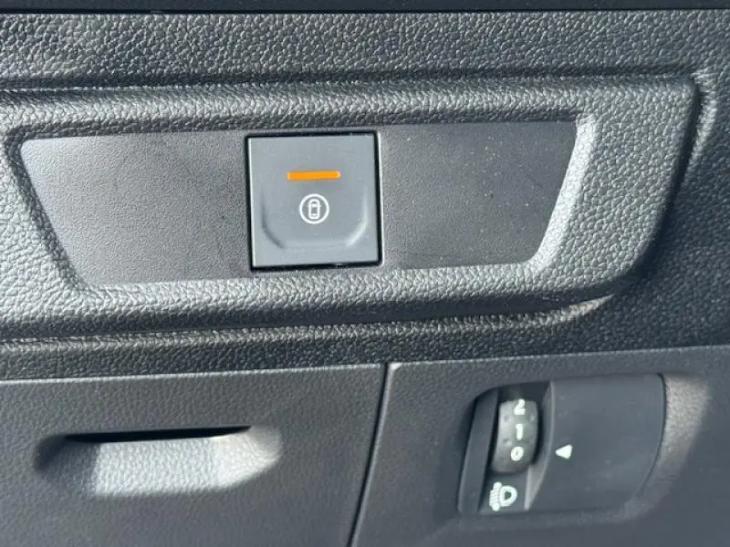 Gros plan sur le bouton de verrouillage centralisé et commande de réglage des phares dans l'habitacle noir d'une Dacia Sandero blanche 2024.