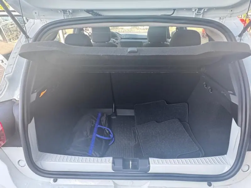 Coffre ouvert vu de l'arrière d'une Dacia Sandero blanche 2024 avec tapis et sac noir à l'intérieur.