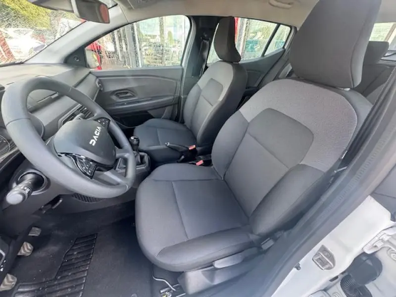 Vue intérieure côté conducteur de la Dacia Sandero blanche 2024, sièges tissu Essential gris et volant multifonction.