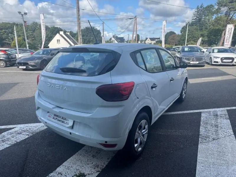 Vue 3/4 arrière droite d'une Dacia Sandero blanche 2024 avec feux arrière rouges et jantes argentées.