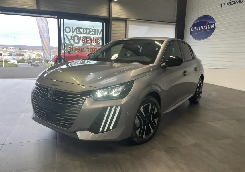 Peugeot 208 gris Artense vue 3/4 avant droit, avec calandre noire et feux LED allumés en showroom.