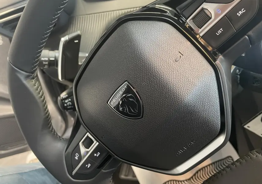 Gros plan sur le volant cuir noir de la Peugeot 208 2025 avec logo lion et commandes intégrées.